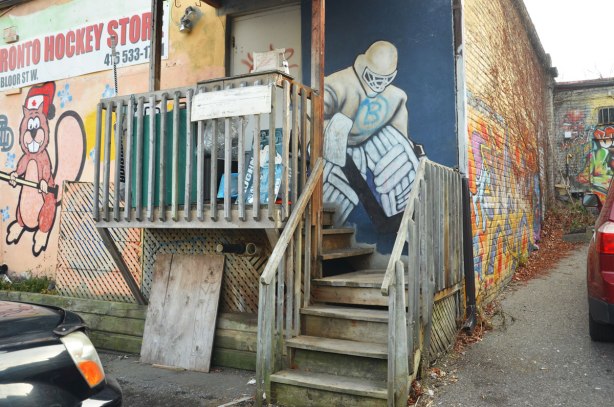 painting of a hockey goalie in full pads and helmet painted on a blue door by a small porch in a laneway.