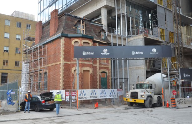 An old three storey brick house, the John Irwin house has been restored and incorporated into a new condo development that is in the process of being built, cement mixer in front, men working. 