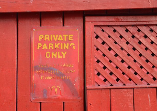 A red sign on a red wall. In yellow letter that are peeling off, the sign says Private Parking Only, mcdonalds.