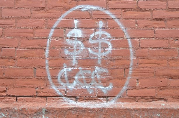 graffiti with two dollar signs and three cent signs on a rust coloured brick wall 
