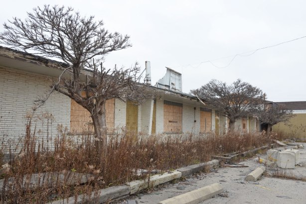 front of abandoned motel Stop 50 on QEW near Hamilton, row of boarded up doors and windows, one storey white brick building 