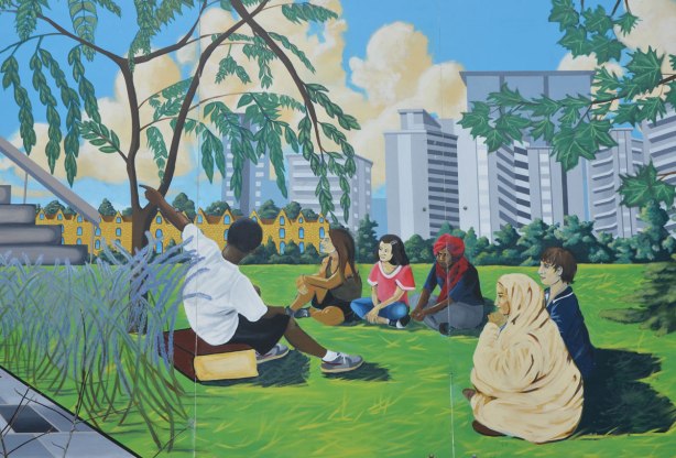 part of a mural celebrating education, a group of people are sitting around in a circle outside while one man is talking