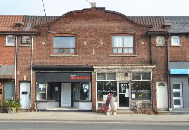 store front, one is an Occult Store, in an old brick building with a curved roofline over the middle of it. 