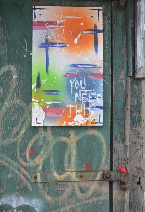An abstract painting with the words you need this written on it. below, tucked into the hinge of the door is a plastic red rose 