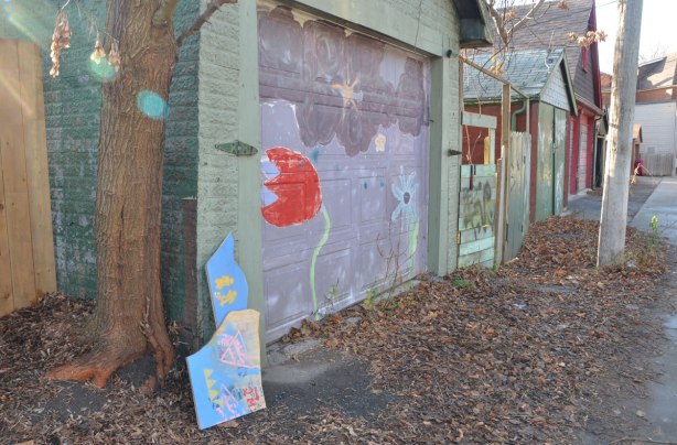 line of garages in an alley. The garage door in the foreground has a bent tulip painted on it. 