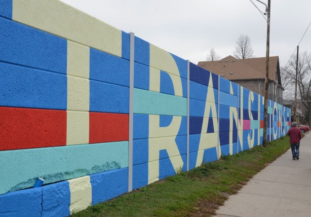 Transitions written in block letters in a large geometric mural that matches the grid of the concrete that makes up the fence