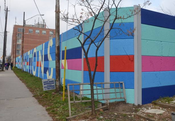 Transitions written in block letters in a large geometric mural that matches the grid of the concrete that makes up the fence
