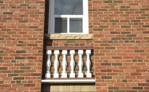 A white framed window in a red brick building. Below the window are a few white pieces of wood that look like a balcony railing even though there is no balcony there. 