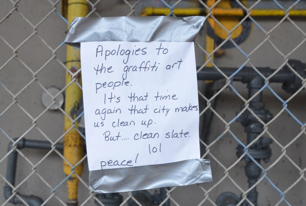 hand written sign duct taped to a chain link fence that reads: Apologies to the graffiti art people. It's that time of year again that city makes us clean up. But... clean slate 101. Peace. 