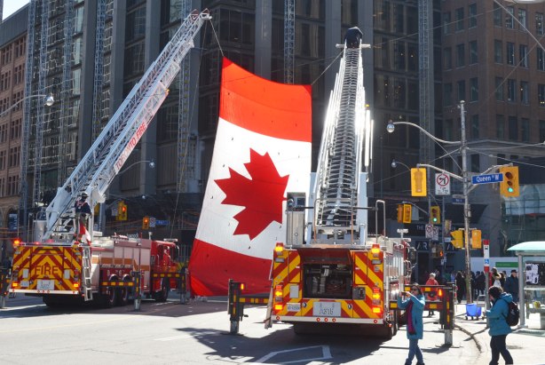 A very large Canadian flag hangs from the cranes of two fire trucks at the corner of Queen and Bay streets in downtown Toronto