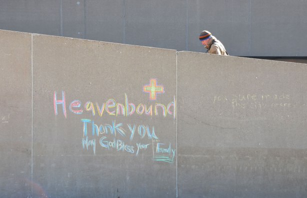 A man walks up the concrete ramp at City Hall, beside him on the wall is written in chalk, Heavenbound. Thankyou. May God bless your family. 