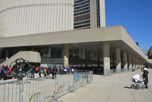 The corner of Toronto City Hall with a long line up of people waiting to get inside. 