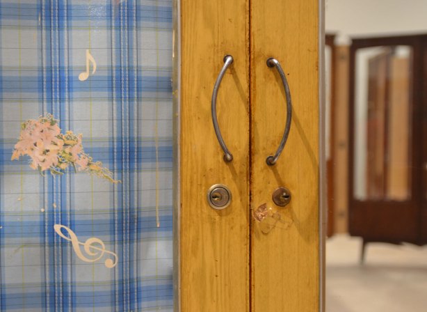 part of an art installation by Chinese artist Song Dong using vintage wooden wardrobe doors with mirrors and curtains, reflections, door handles, key holes and a curtain that is a blue and white plaid and has musical notes on it. 