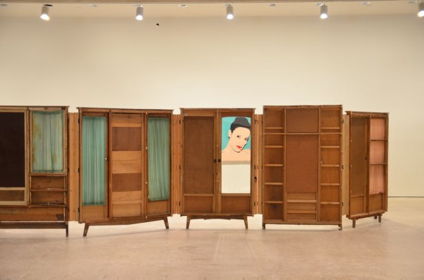 part of an art installation by Chinese artist Song Dong using vintage wooden wardrobe doors with mirrors and curtains, reflections. through one of the windows there is a painting of Karen Kain on the wall 