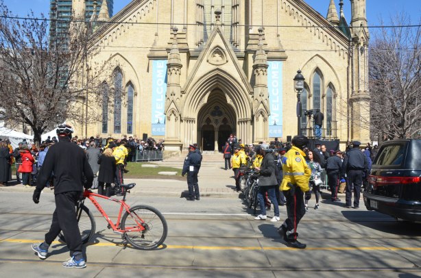 From King St., the view of St. James cathedral front doors, lots of people and police in yellow jackets in the picture as well as a man walking his bike