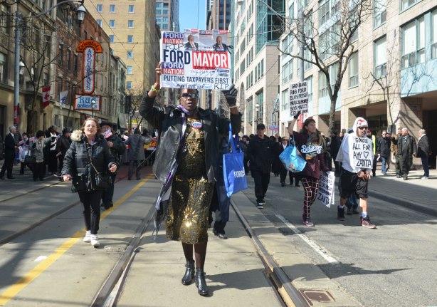 a woman holding a ford nation sign above her head walks in a procession across King street
