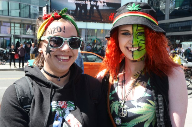 Part of 420 day celebrations at Dundas Square - two young women are dressed up in cannabis themed clothes with make up on their faces. One woman has 420! written on her forehead, the other woman has half her face painted green 