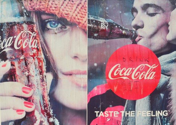 A large poster coca-cola ad. In the red circle with the coke logo, has been written in black, drink and get fat, such that the sign now says, drink coca-cola, get fat. 