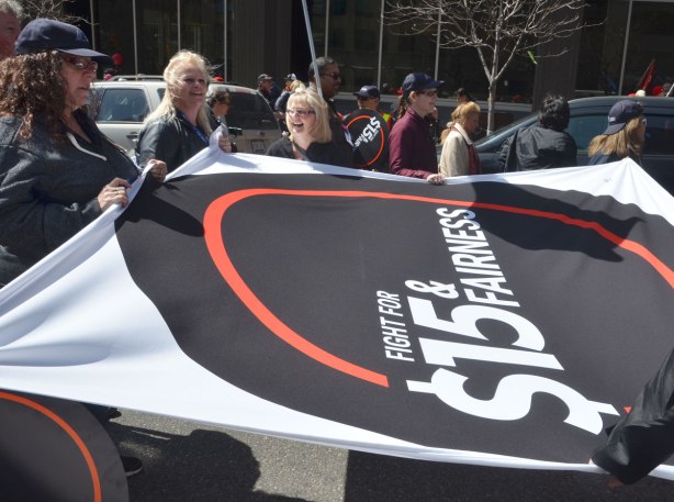 photographs taken at a rally and protest in support of a $15 minimum wage, The Fight for 15 and fairness - a group of people stand around holding a flag banner about 3 metres by 3 metres that says fight for fifteen and fairness. 