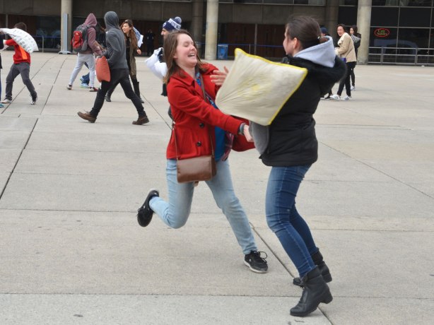 two young women leaping at each other as they try to hit each other with pillows