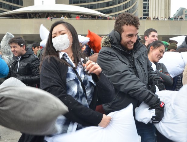 people in the midst of a large pillow fight at Nathan Phillips square in celebration of international pillow fight day - a young man with earmuffs and a woman wearing a face mask