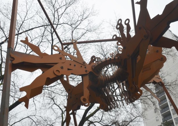 close up of a sculpture of flat metal people shapes, forming a circle with their heads, their feet sticking out like in a centrifuge. 