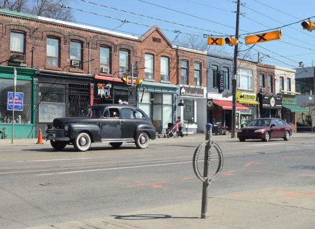 A black vintage car drives by on Queen St East