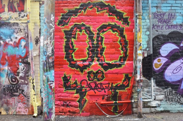 alley laneway streetart by artist PK of a stylized face, or could be a skull - black outlines of top of skull, eyes, nose holes, and sort of teeth, on red background