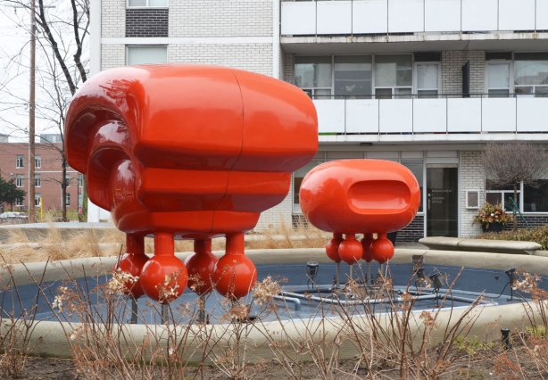 sculpture in front of an apartment building, two red shiny things that look like alien spaceships