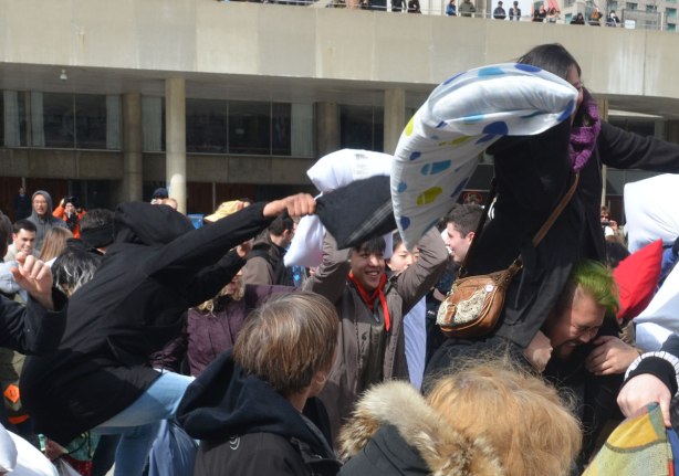 people in the midst of a large pillow fight at Nathan Phillips square in celebration of international pillow fight day - a young woman is on the shoulders of a man as they pass through a crowd during a pillow fight