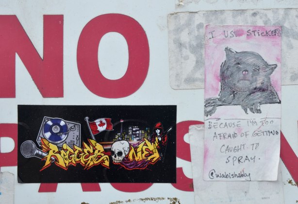 A very small hand printed sticker that has been stuck to a sign on a wall, top part of sticker is picture of a cat, bottom half of sticker are the words: "