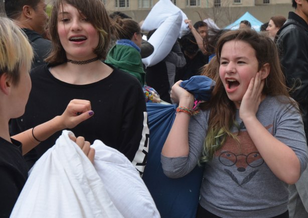 a young woman holding a pillow and screaming at another young woman