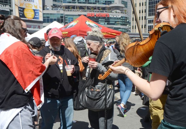 three older people share joints while a red haired woman plays a violin, Dundas Square, 420 day event