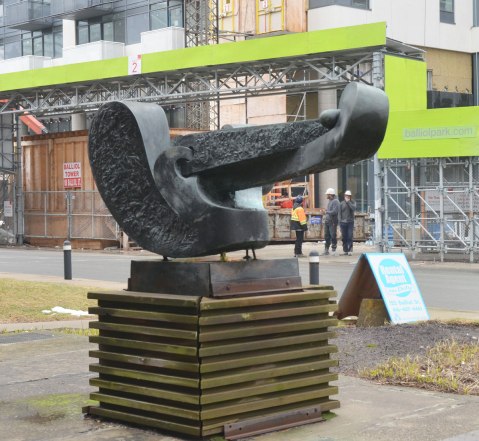 Grand Odalisque, a sculpture by Sorel Ertog sits on a wood pedestal . Looking across Balliol from behind the sculpture. The scene across the street is a few men standing in front of a construction site where a new condo is being built