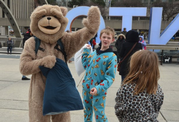a person in a bear costume waves to the camera as a boy in pyjamas holds a pillow