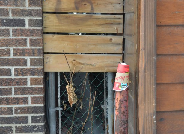 an empty paper coffee cup from Tim Hortons that has been discarded - upside down on top of a metal pole that is about a meter high, in an alley, beside a gate