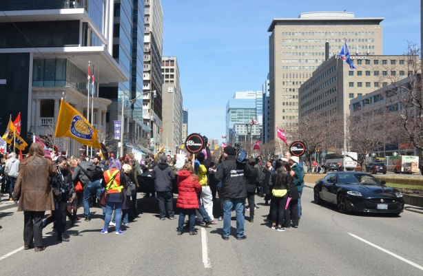 photographs taken at a rally and protest in support of a $15 minimum wage, The Fight for 15 and fairness - the rally spilled onto the street at one point. police kept the far lane open for traffic, in this picture an upmarket car (Jaguar?) passes by the crowd 