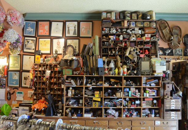 Against a wall in Gadabout store, shelves with small cubbyholes all filled with small items, curios, b=vintage, treasures, such as old producs, toys, figurines, household items,