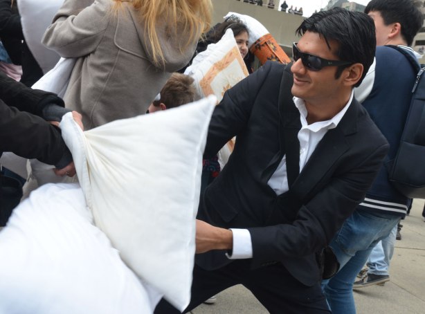 people in the midst of a large pillow fight at Nathan Phillips square in celebration of international pillow fight day - a man wearing a suit and dark sunglasses participates in the pillow fight