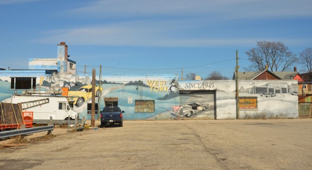 mural on the side of West York motors on St. Clair West - a view of the mural from across the almost empty parking lot. 