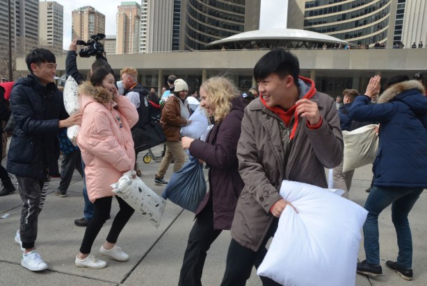 people in the midst of a large pillow fight at Nathan Phillips square in celebration of international pillow fight day - a number of young people laughing