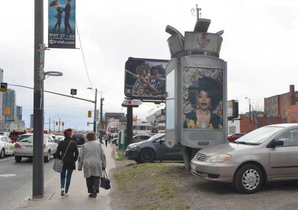 Two women walk past part of an art installation, portrait of a black woman on a billboard, by Mickalene Thomas, in a parking lot in downtown Toronto