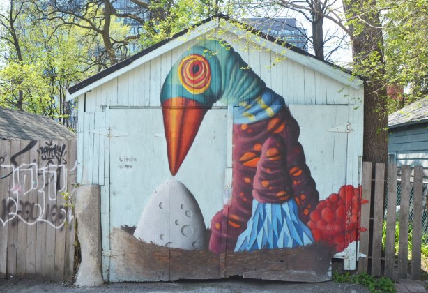 street art mural on a garage door in an alley by birdo - a large bird with blue head and orange beak sitting in a nest looking down at a large white egg