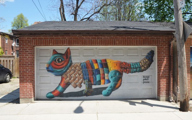 street art mural on a garage door in an alley by birdo - a large multicoloured cat. words: tense phil pans