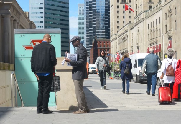 A man is selling Black History newspaper to another man in front of the TTC subwayentrance at Union station. 