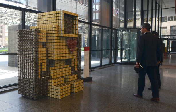 A large 3D lovebot, about 6 feet tall, made of canned food stands in the lobby of the TD centre, it's an entry in the Canstruction event. Two men in suits are looking at it. 
