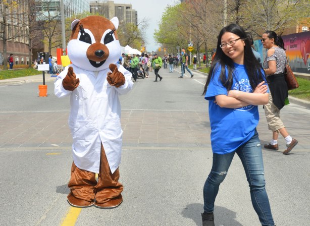 A person dressed in a costume that looks like an animal - squirrel? fox? that is wearing a lab coat. An Asian woman who was walking with him before the photo was taken is shyly turning away, she is also laughing