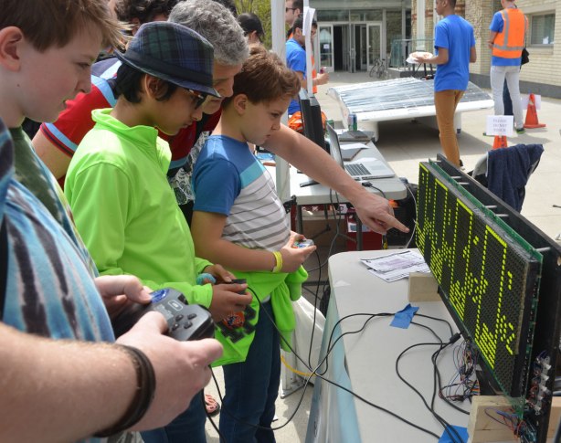 Three young man are playing a tetris game on a large computer board. 