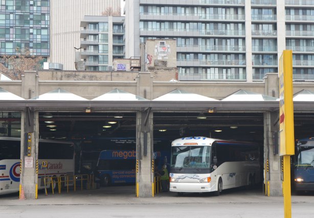 large lovebot wheatepaste paste up above the downtown Toronto bus terminal. A white bus is parked in one of the bus bays. Condos in the background. 