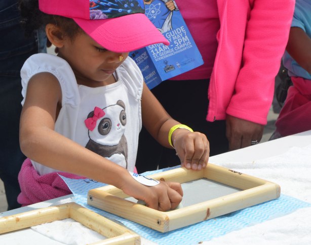 a young girl is making paper. she is sponging the paper dry over a piece of mesh in a frame